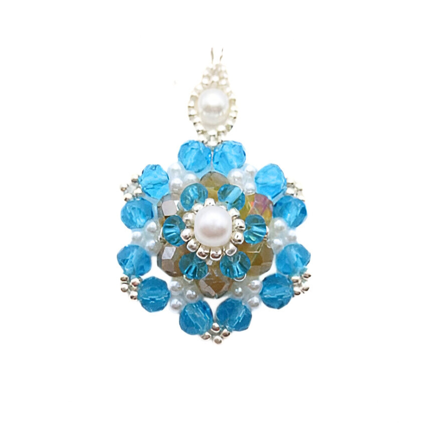 Handmade large statement pendant featuring vivid aquamarine blue faceted crystals, an iridescent golden centre crystal, white pearls and silver bead accents, with a decorative white pearl and silver bail, displayed on a silver-tone chain against a white background.