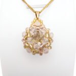 Handmade champagne crystal cluster pendant featuring a large champagne faceted centre crystal surrounded by clear crystals, golden yellow bead accents, with a gold-tone bail, displayed on a gold-tone curb chain and white jewellery stand.