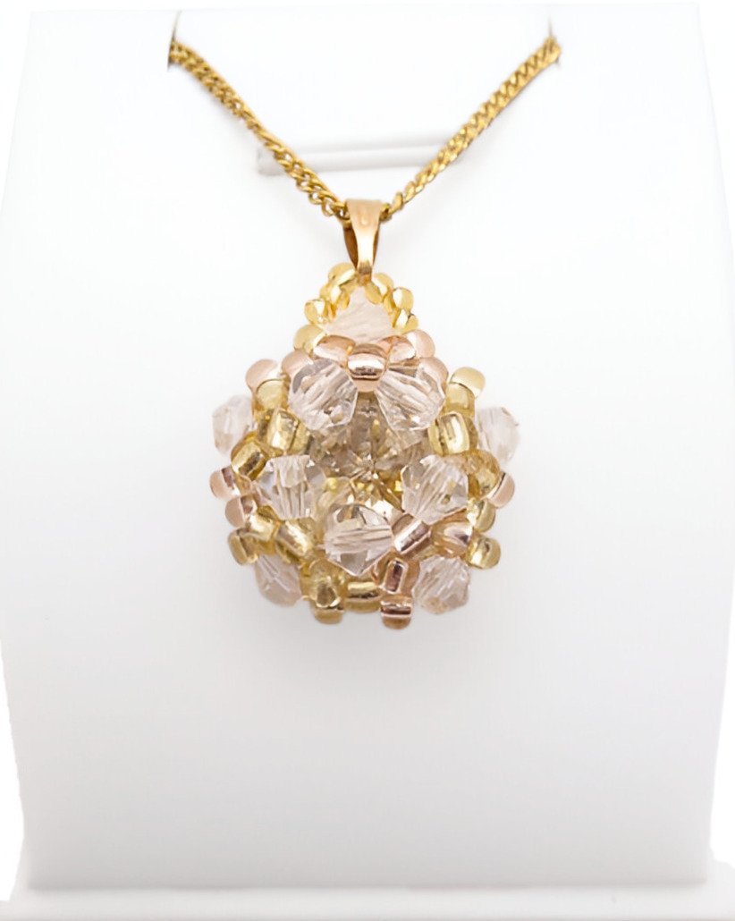 champagne-crystal-pendant-display Handmade champagne crystal cluster pendant featuring a large champagne faceted centre crystal surrounded by clear crystals, golden yellow bead accents, with a gold-tone bail, displayed on a gold-tone curb chain and white jewellery stand.