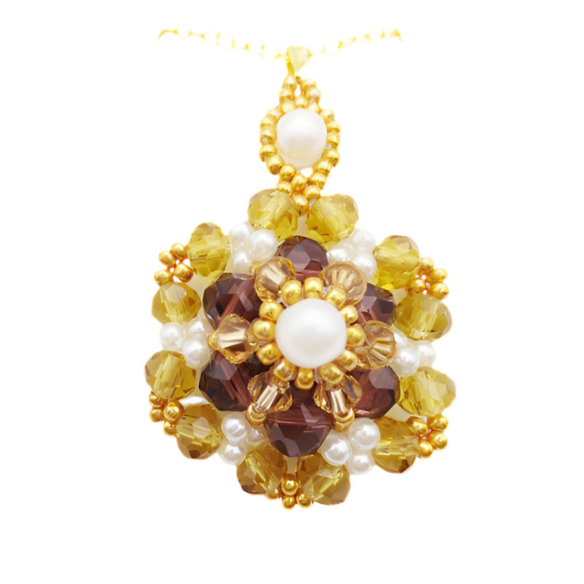 Handmade large statement pendant featuring rich amber and golden faceted crystals, a white pearl centre, white seed pearl accents and gold seed bead detailing throughout, with a decorative pearl and gold bail, displayed on a gold-tone chain and white jewellery stand.