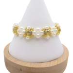 Handmade beaded bracelet featuring faceted golden yellow crystal beads surrounded by clusters of white pearl beads and small gold-tone seed bead accents, displayed on a white cone jewelry stand with wooden base