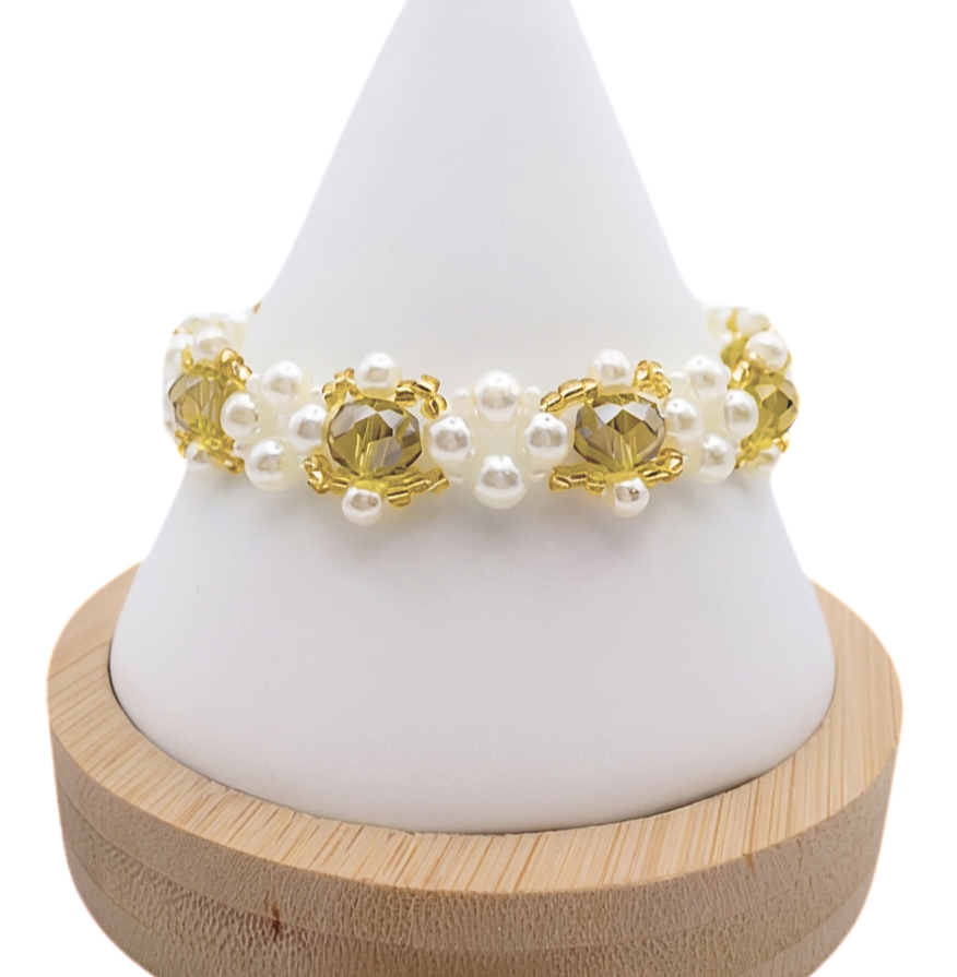 Handmade beaded bracelet featuring faceted golden yellow crystal beads surrounded by clusters of white pearl beads and small gold-tone seed bead accents, displayed on a white cone jewelry stand with wooden base