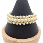 Handmade wide beaded bracelet featuring multi-sized white pearl beads woven together with gold-tone beads in a textured layered pattern, displayed on a black cone jewellery stand with wooden base