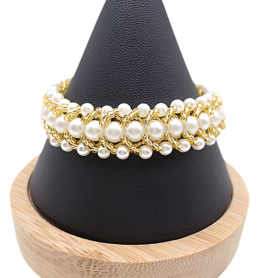 pearl-gold-bead-bracelet-main Handmade wide beaded bracelet featuring multi-sized white pearl beads woven together with gold-tone beads in a textured layered pattern, displayed on a black cone jewellery stand with wooden base