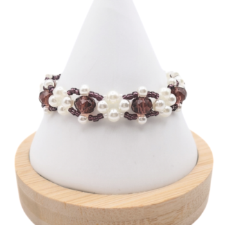 Handmade beaded bracelet featuring faceted deep purple crystal beads surrounded by clusters of white pearl beads and small purple seed bead accents, displayed on a white cone jewelry stand with wooden base.