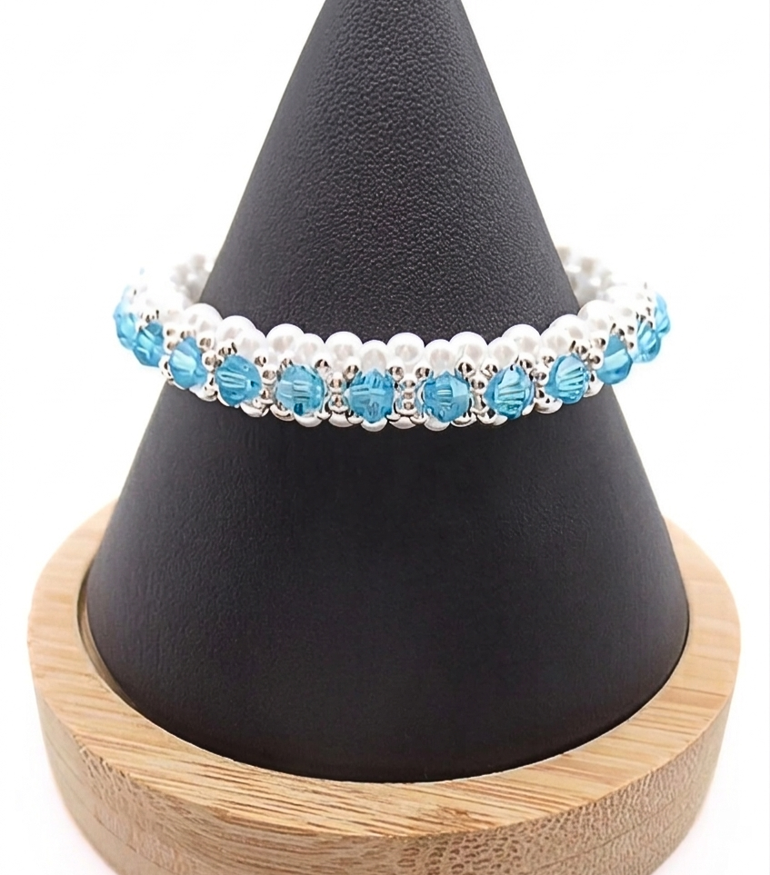 aquamarine-bracelet-cone-dispaly Handmade beaded bracelet featuring aquamarine blue crystal beads, white pearl beads, and silver-tone accent beads, displayed on a black cone jewelry stand with wooden base