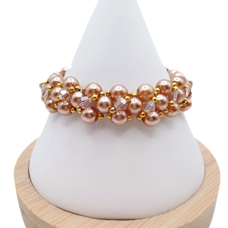 Handmade bracelet featuring lustrous light brown champagne pearls woven together with champagne faceted crystals and gold bead accents in a full rounded cluster design, displayed on a white cone bracelet stand with a wooden base against a white background.