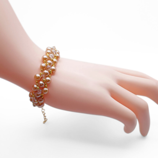 Handmade light brown champagne pearl bracelet with champagne crystals and gold bead accents in a full rounded cluster weave, with a gold-tone extension chain clasp, shown worn on a mannequin wrist against a white background.
