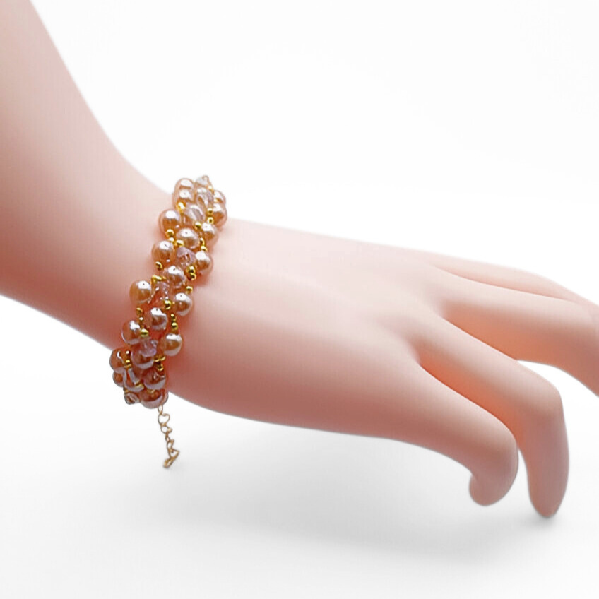 Handmade light brown champagne pearl bracelet with champagne crystals and gold bead accents in a full rounded cluster weave, with a gold-tone extension chain clasp, shown worn on a mannequin wrist against a white background.