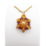 Crystal and pearl pendant with a champagne centre pearl surrounded by warm champagne faceted crystals and an outer purple crystals, accented throughout with gold beads, displayed on a gold-tone curb chain and white jewellery stand.