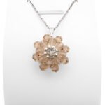 Champagne Crystal Pendant: Handmade champagne crystal flower pendant with two layers of warm golden-pink faceted crystals and a sparkling cubic zirconia centre, displayed on a silver-tone chain and white jewellery stand.