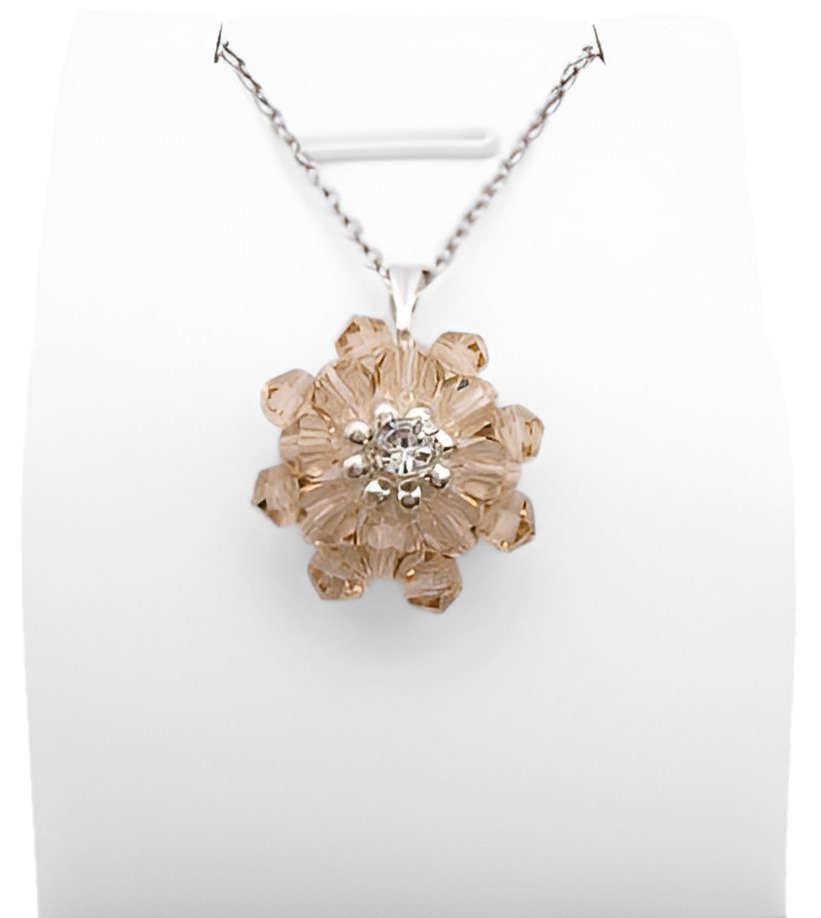 cubic-zirconia-champangne-pendant-display Champagne Crystal Pendant: Handmade champagne crystal flower pendant with two layers of warm golden-pink faceted crystals and a sparkling cubic zirconia centre, displayed on a silver-tone chain and white jewellery stand.