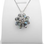 Handmade grey crystal AB flower pendant with two layers of iridescent grey-blue aurora borealis faceted crystals and a sparkling cubic zirconia centre, displayed on a silver-tone chain and white jewellery stand.