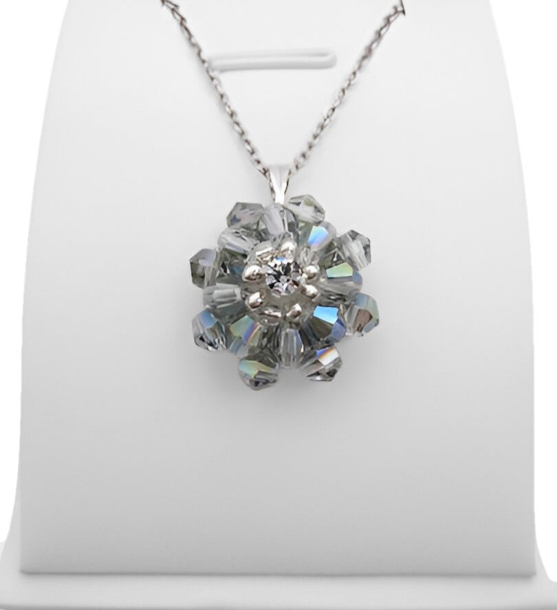 cubic-zirconia-grey-pendant-display Handmade grey crystal AB flower pendant with two layers of iridescent grey-blue aurora borealis faceted crystals and a sparkling cubic zirconia centre, displayed on a silver-tone chain and white jewellery stand.