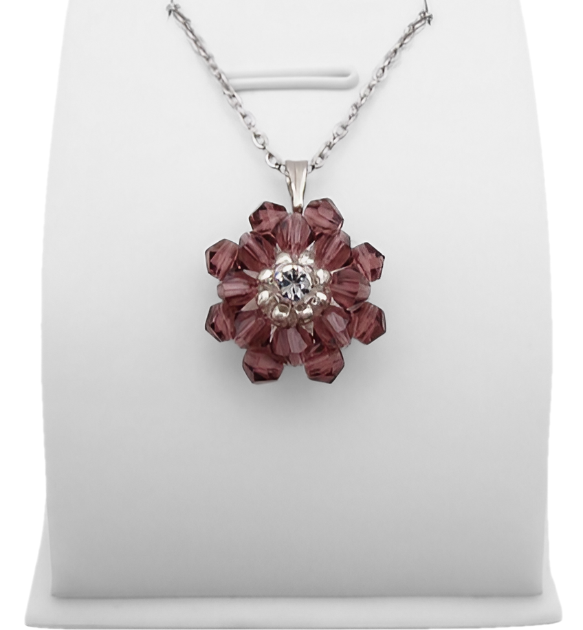 cubic-zirconia-purple-pendant-display Handmade purple crystal flower pendant with two layers of iridescent grey-blue aurora borealis faceted crystals and a sparkling cubic zirconia centre, displayed on a silver-tone chain and white jewellery stand.