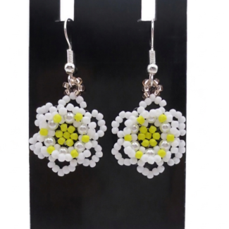A pair of handmade white and yellow beaded daisy flower earrings hanging on a black metal earring display stand against a white background.