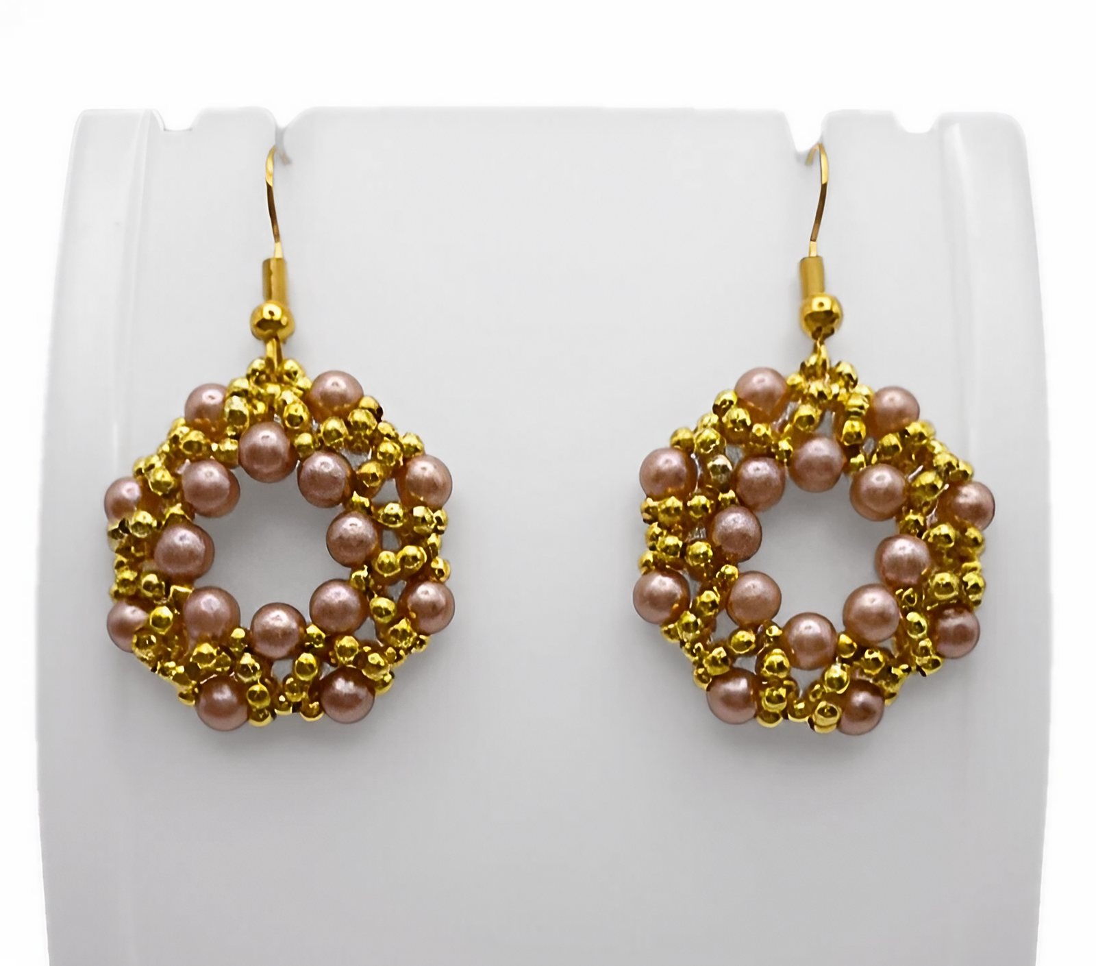 Handmade light brown faux pearl and gold-tone beaded open hoop drop earrings displayed on a white earring stand, showcasing the full woven circular lattice shape and gold fish hook ear wires