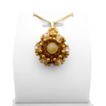 Handmade golden tourmaline pendant featuring a smooth round yellow tourmaline centre stone surrounded by warm amber and champagne faceted crystals with gold seed accents, displayed on a gold-tone curb chain and white jewellery stand.