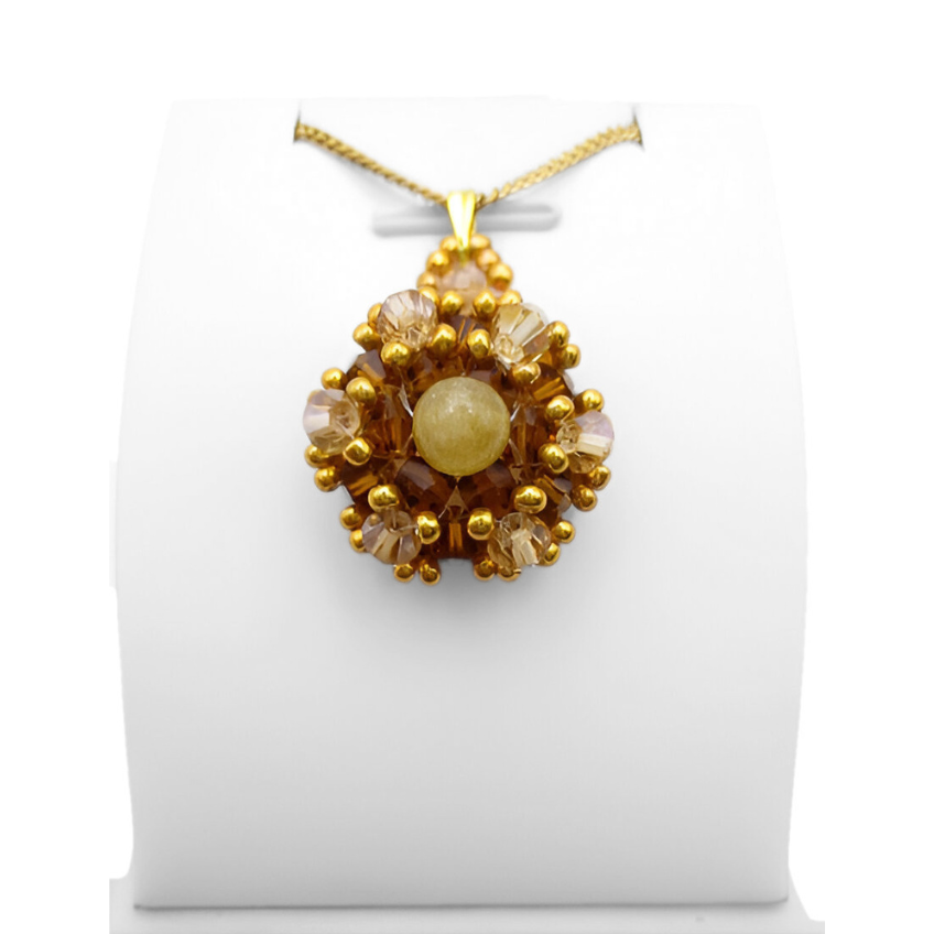 golden-tourmaline- pendant-display Handmade golden tourmaline pendant featuring a smooth round yellow tourmaline centre stone surrounded by warm amber and champagne faceted crystals with gold seed accents, displayed on a gold-tone curb chain and white jewellery stand.