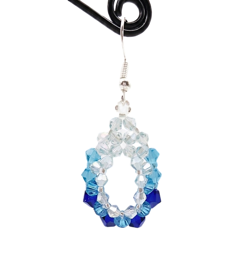 Detailed view of handmade blue ombre gradient crystal oval dangle earring on display stand, light blue to navy beaded open hoop, silver wire hook, shown against a white background.