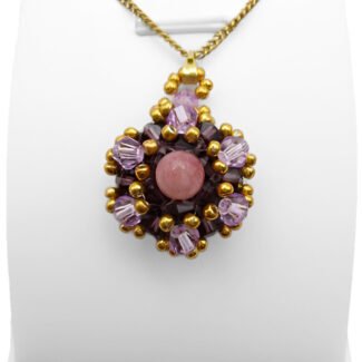 Handmade pink tourmaline pendant featuring a smooth round pink tourmaline centre stone surrounded by deep violet and light purple faceted crystals with gold bead accents and a gold-tone bail, shown on a white jewellery stand.