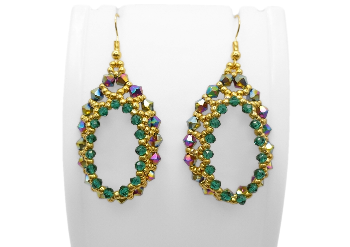 teardrop-hoop-earrings-display Emerald green and gold beaded teardrop hoop earrings displayed on a white jewellery stand, featuring iridescent rainbow crystals and gold seed beads with gold-tone ear wires.