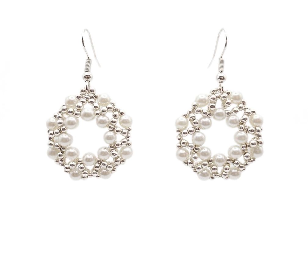 Handmade open hoop drop earrings featuring woven white faux pearl beads and silver-tone accent beads in a circular lattice design, with silver-tone fish hook ear wires — flat lay view