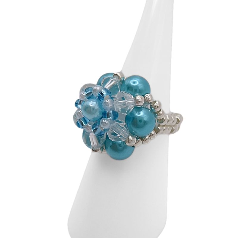 aquamarine-pearl-ring-close-up A side view of a handmade aquamarine pearl and crystal cluster ring on white cone ring stand — sky blue pearl beads, clear crystals, and silver-tone seed bead band