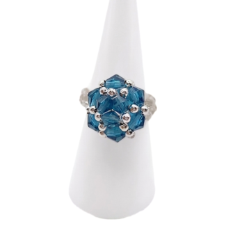 Front view of handmade ocean blue crystal cluster cocktail ring on white cone ring stand — faceted blue crystals and silver-tone bead accents, geometric cluster design
