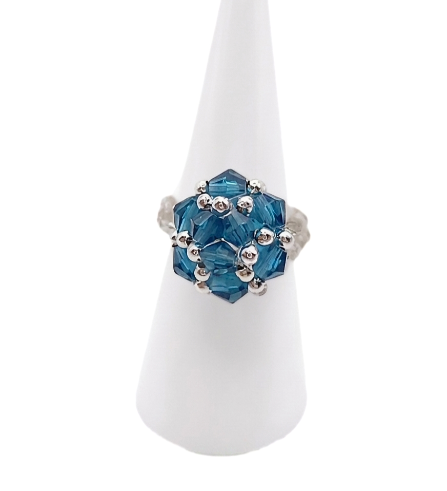Front view of handmade ocean blue crystal cluster cocktail ring on white cone ring stand — faceted blue crystals and silver-tone bead accents, geometric cluster design