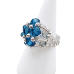 Angled side view of handmade ocean blue and clear crystal cluster ring on white cone display stand — faceted ocean blue crystals, clear rod crystals, and silver-tone beaded band