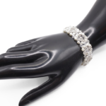 Bridal bracelet featuring white pearls and clear faceted crystals with silver-tone bead accents in a repeating floral pattern, shown on a black mannequin hand against a white background.