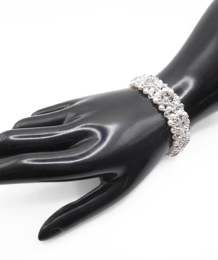 Bridal bracelet featuring white pearls and clear faceted crystals with silver-tone bead accents in a repeating floral pattern, shown on a black mannequin hand against a white background.
