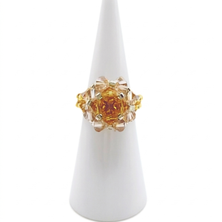 Handmade crystal beaded cocktail ring with amber topaz center crystals and surrounding champagne crystals on gold beaded band, displayed on white cone ring holder