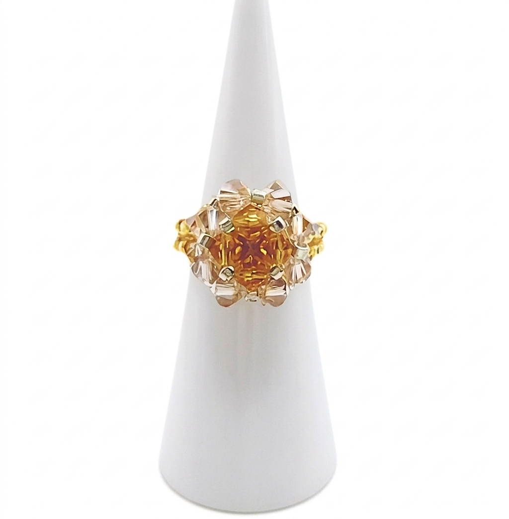 champagne-crystal-ring-display Handmade crystal beaded cocktail ring with amber topaz center crystals and surrounding champagne crystals on gold beaded band, displayed on white cone ring holder