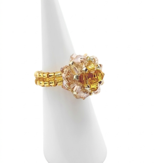 Handmade beaded ball ring with golden topaz and blush champagne crystals on gold beaded band, shown on white ceramic ring display cone