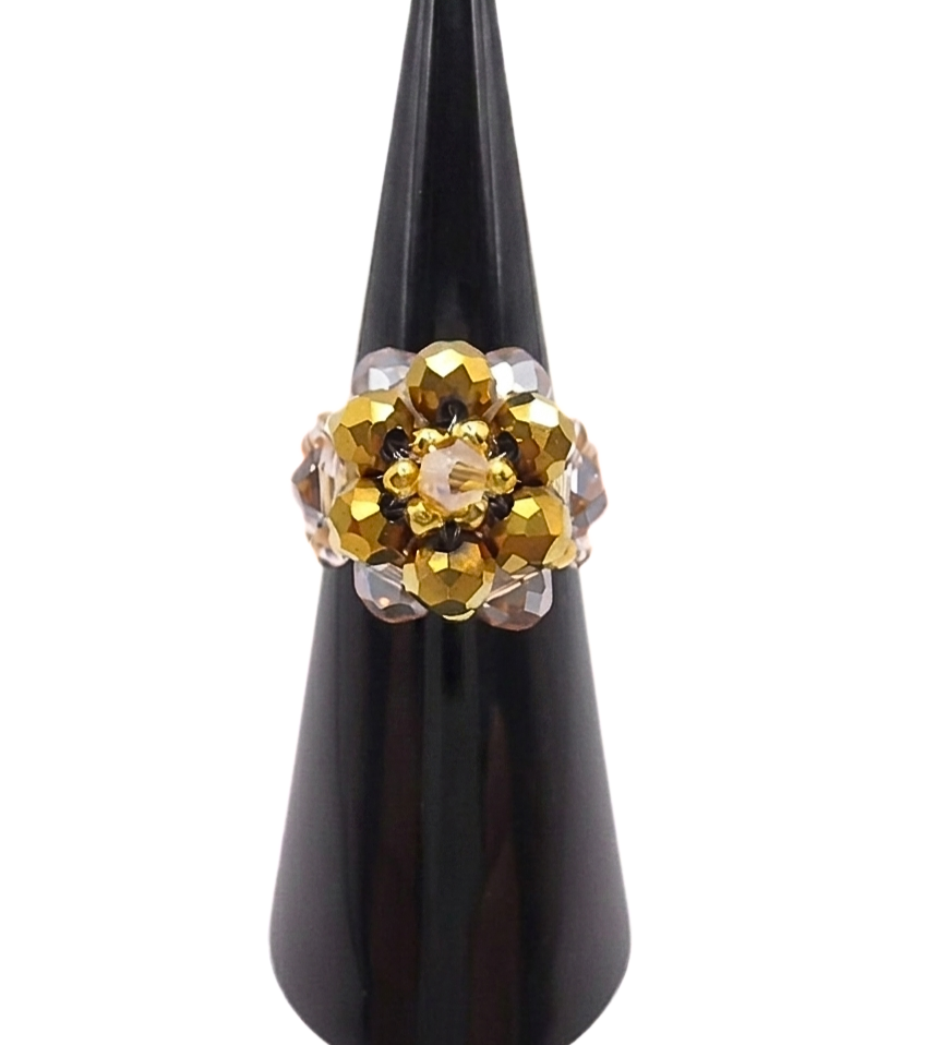 Handmade beaded cocktail ring featuring a domed cluster of metallic gold and champagne crystal beads in a floral design, displayed on a black cone ring stand against a white background