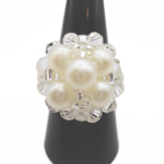 White pearl cluster cocktail ring with clear crystal accents displayed on black ring cone stand - handmade beaded statement ring