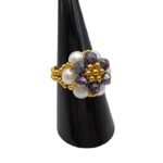 Handmade cluster ring featuring white pearl beads, faceted purple AB crystal beads, and gold-tone metal accents on a beaded stretch band, displayed on a black ring cone — side view