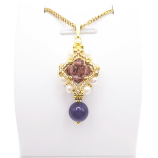 Handmade purple drop pendant necklace featuring a diamond-shaped top section with purple faceted crystals, white pearls and gold beads, suspending a smooth violet gemstone drop bead, displayed on a gold-tone curb chain and white jewellery stand.