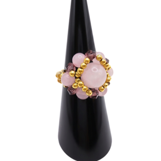Angled view of a handmade rose quartz beaded cluster ring with purple crystal beads and gold-tone accent beads on a stretch band, displayed on a black ring cone