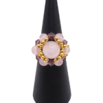 Front view of a handmade cluster ring featuring a large rose quartz center bead, smaller rose quartz beads, faceted purple crystal beads, and gold-tone metal accent beads, displayed on a black ring cone