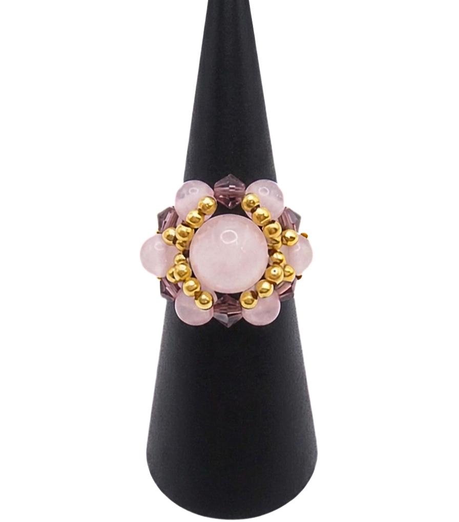 Front view of a handmade cluster ring featuring a large rose quartz center bead, smaller rose quartz beads, faceted purple crystal beads, and gold-tone metal accent beads, displayed on a black ring cone