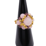 Side view of a handmade rose quartz beaded cluster ring with purple crystal beads and gold-tone accent beads on a stretch band, displayed on a black ring cone
