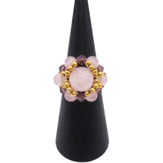Handmade cluster ring featuring a large rose quartz center bead, smaller rose quartz beads, faceted purple crystal beads, and gold-tone metal accent beads, displayed on a black ring cone