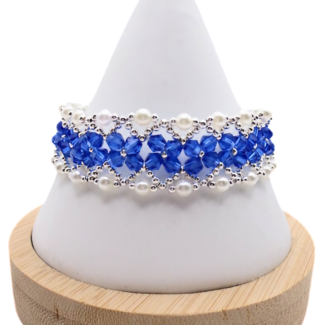Elegant bracelet featuring vivid royal blue faceted crystals forming a central band bordered by white pearls and silver-tone bead accents in a repeating diamond pattern, displayed on a white bracelet stand against a white background.