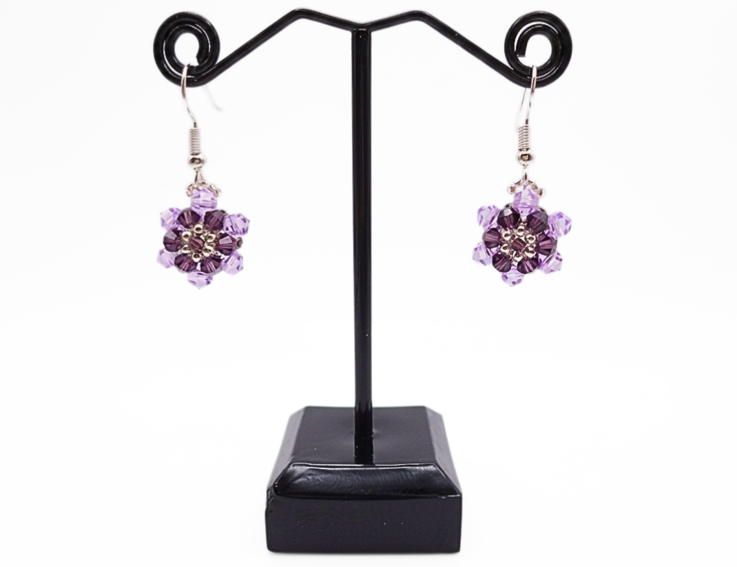 crystal-floral-earrings-black-display Lilac and purple crystal flower drop earrings hanging on a black metal jewellery stand against a white background