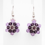 Purple crystal floral earrings displayed on a white jewellery stand, showing layered lilac and dark purple crystal flower design
