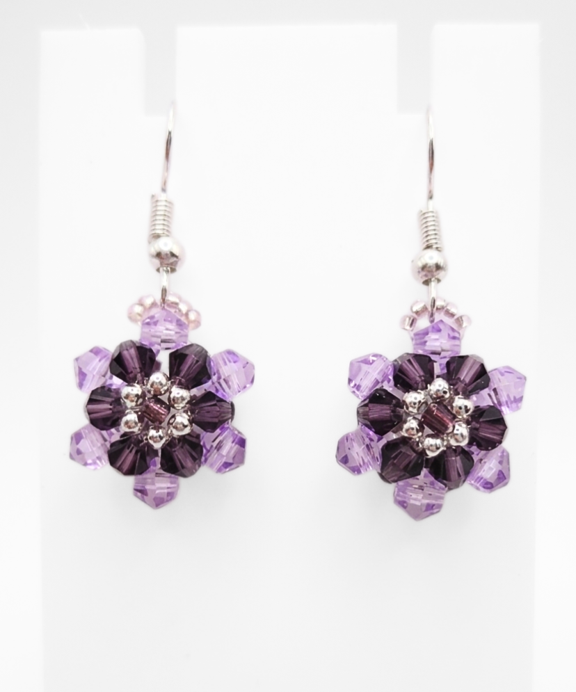 crystal-floral-earrings-white-display Purple crystal floral earrings displayed on a white jewellery stand, showing layered lilac and dark purple crystal flower design
