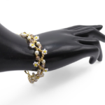 Handmade delicate daisy bracelet featuring white seed bead daisy flowers with yellow centres, white pearls, champagne crystals and gold seed bead accents woven in an open floral chain design with a gold-tone extension clasp, shown worn on a black mannequin hand against a white background.